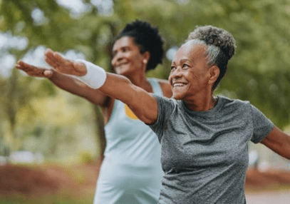 Two elderly women practicing yoga outdoors, smiling and stretching.