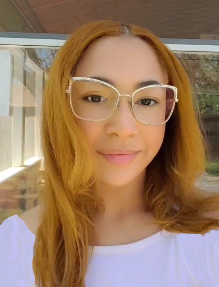 Young woman with long hair and glasses smiling indoors.