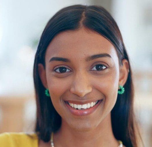 A smiling young woman with straight black hair and turquoise earrings.